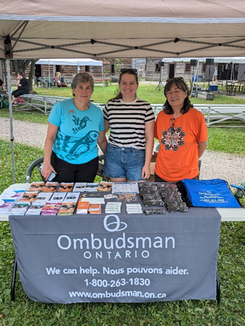 Ombudsman Ontario staff members standing behind a table filled with Ombudsman giveaways and information materials, such as reports, lapel pins and brochures.