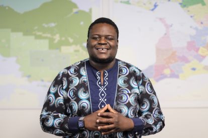 Staff photo - Mobolaji Staff member smiling at the camera in front of a map of Ontario.