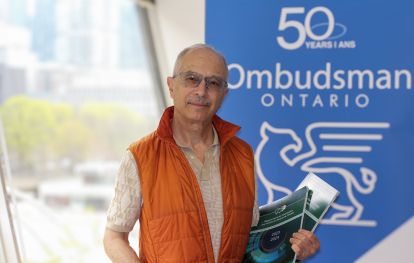 Staff photo - Toufic Staff member smiling with banner that says 50 Years of Ombudsman Ontario in the background.